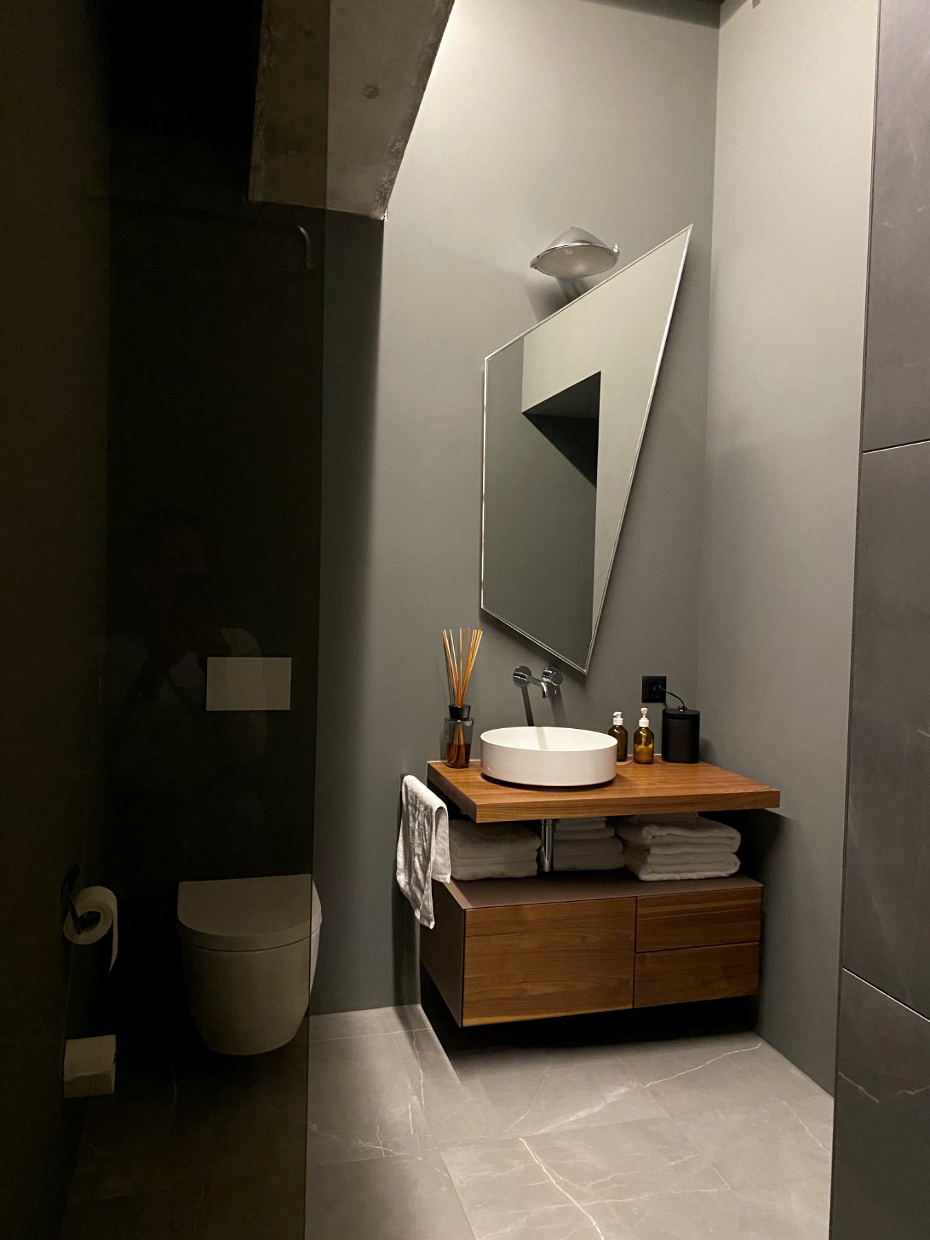Guest bathroom with single angular mirror, wood vanity and concrete ceiling
