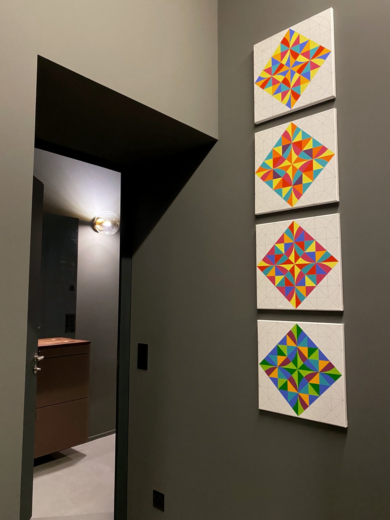 Vestibule with four stacked geometric paintings on dark green wall and view through doorway