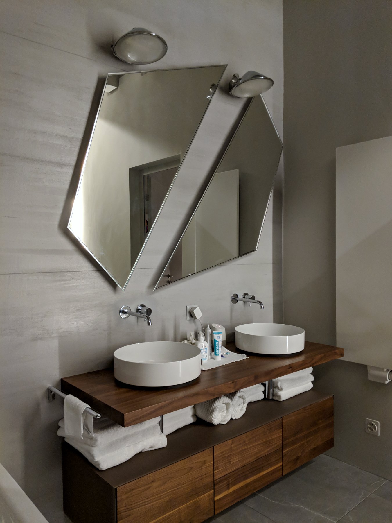 Master bathroom paired angular mirrors above walnut double-sink vanity