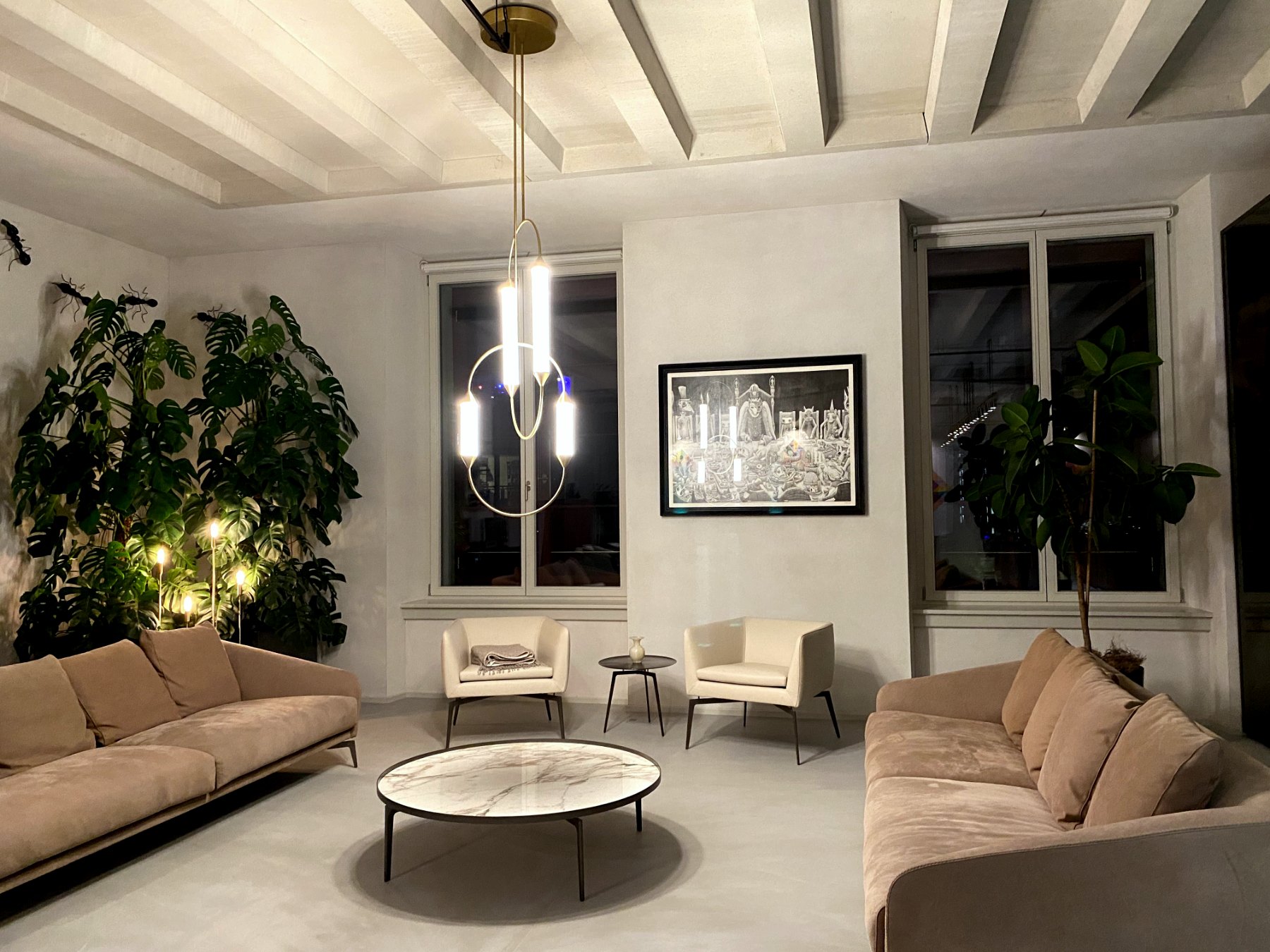 Salon with brass ring chandelier, two beige sofas, plants and round marble coffee table